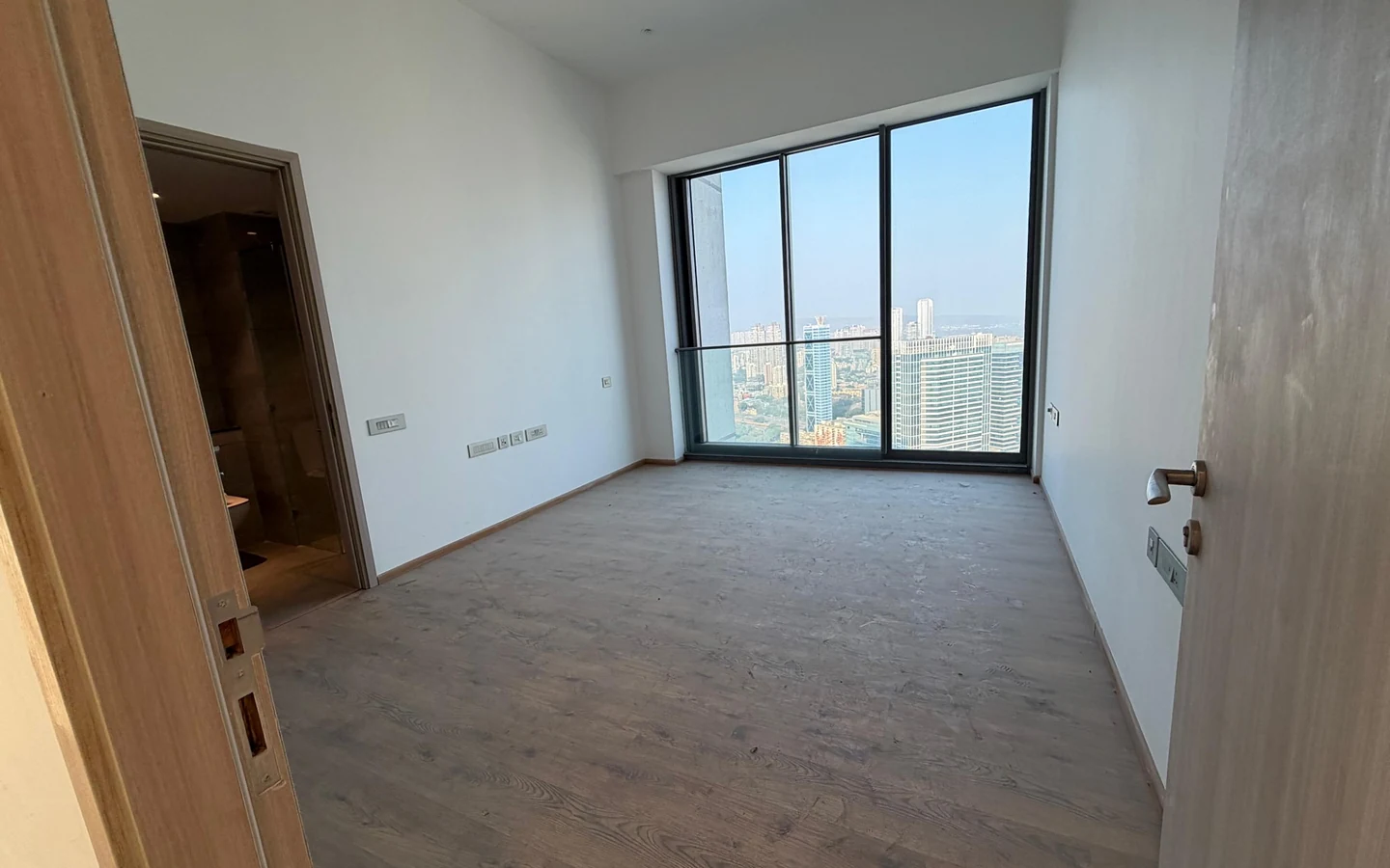 Master bedroom with wooden flooring, attached bathroom and floor-to-ceiling city view windows in 5 BHK at Rustomjee Crown, Prabhadevi
