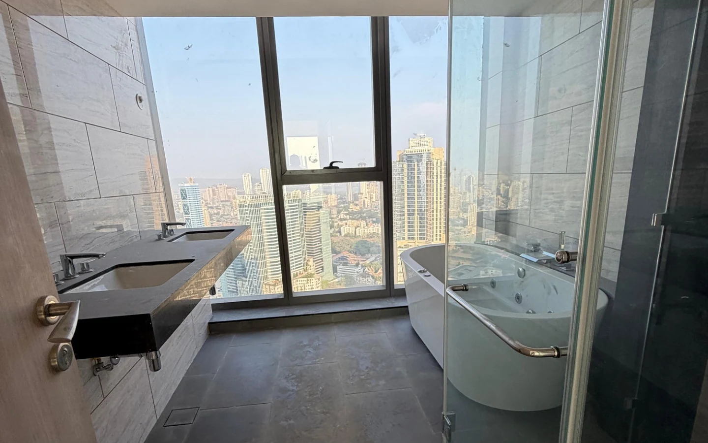 Master bathroom with jacuzzi bathtub, twin-sink vanity and full-height city view window at Rustomjee Crown, Prabhadevi