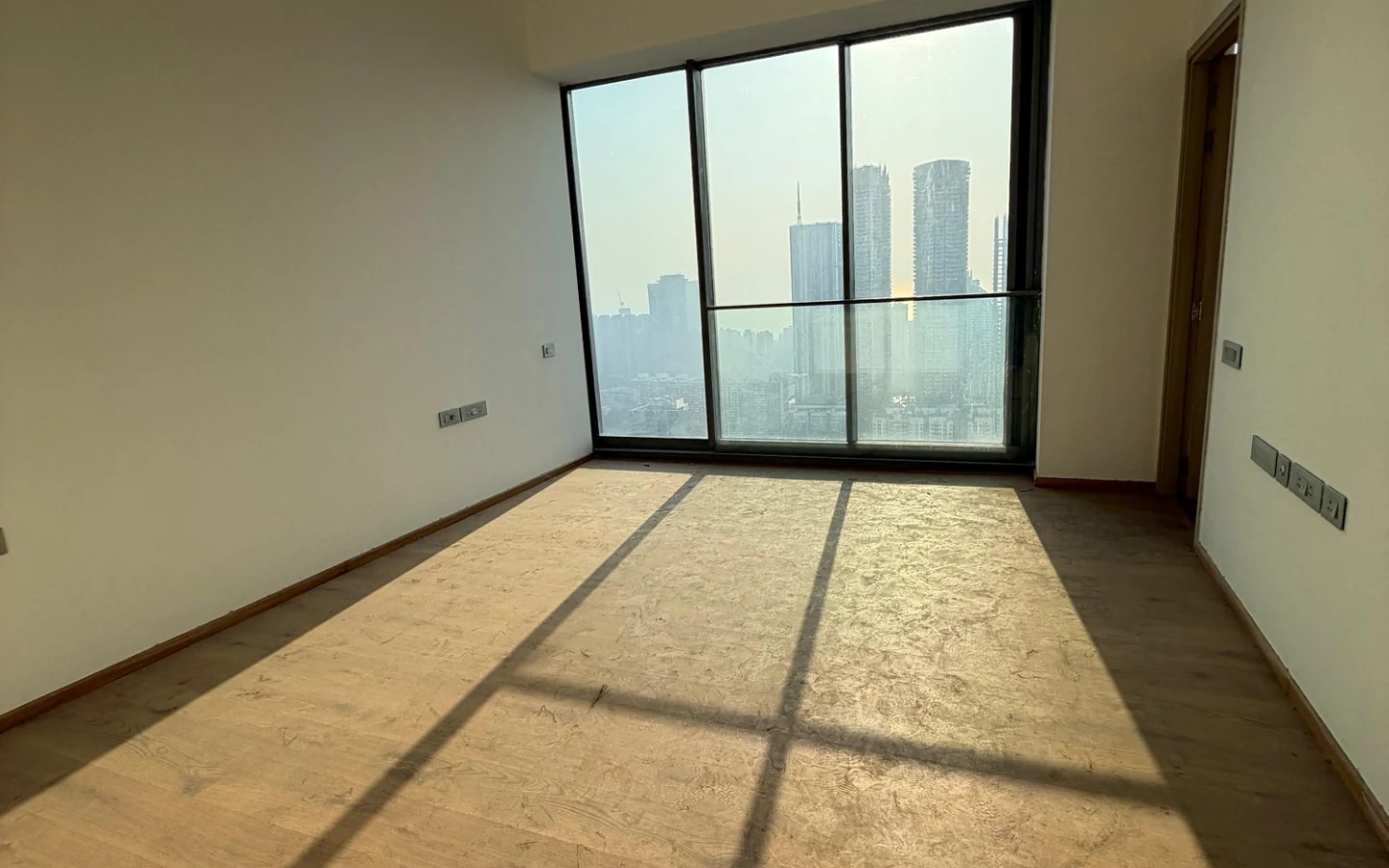 Sunlit bedroom with wooden flooring and floor-to-ceiling window with high-rise view at Rustomjee Crown, Prabhadevi