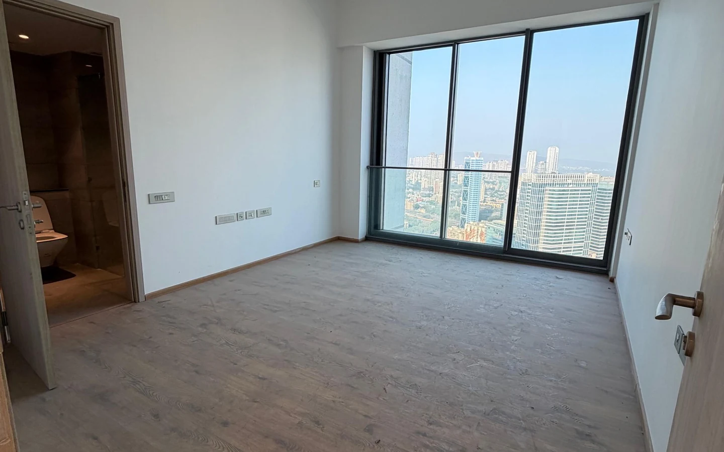 Bedroom with attached bathroom, wooden flooring and large city view window in 5 BHK at Rustomjee Crown, Prabhadevi