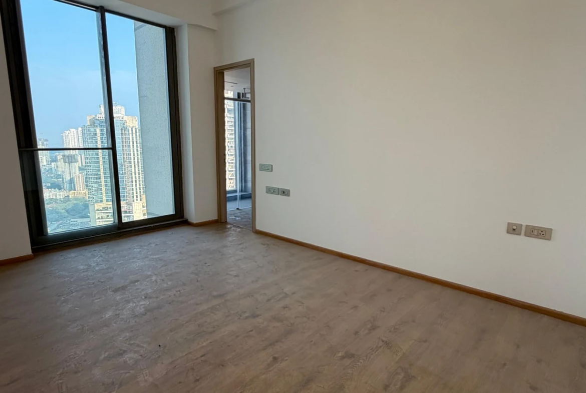 Bedroom with wooden flooring and tall glass window overlooking the city at Rustomjee Crown, Prabhadevi