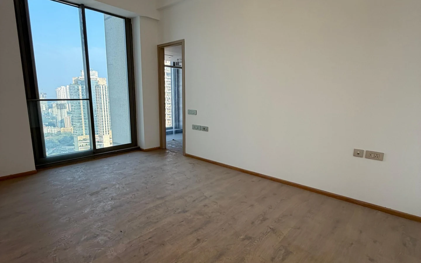 Bedroom with wooden flooring and tall glass window overlooking the city at Rustomjee Crown, Prabhadevi