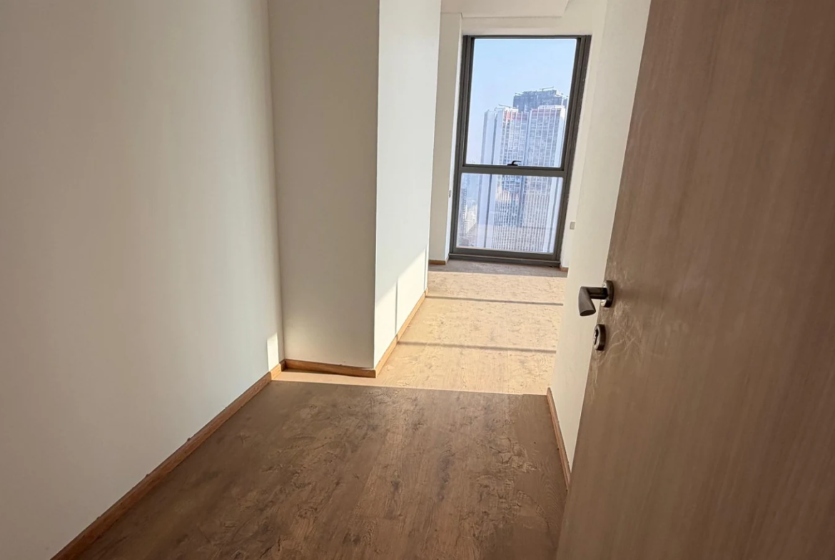 Passage with wooden flooring leading to a floor-to-ceiling window at Rustomjee Crown, Prabhadevi