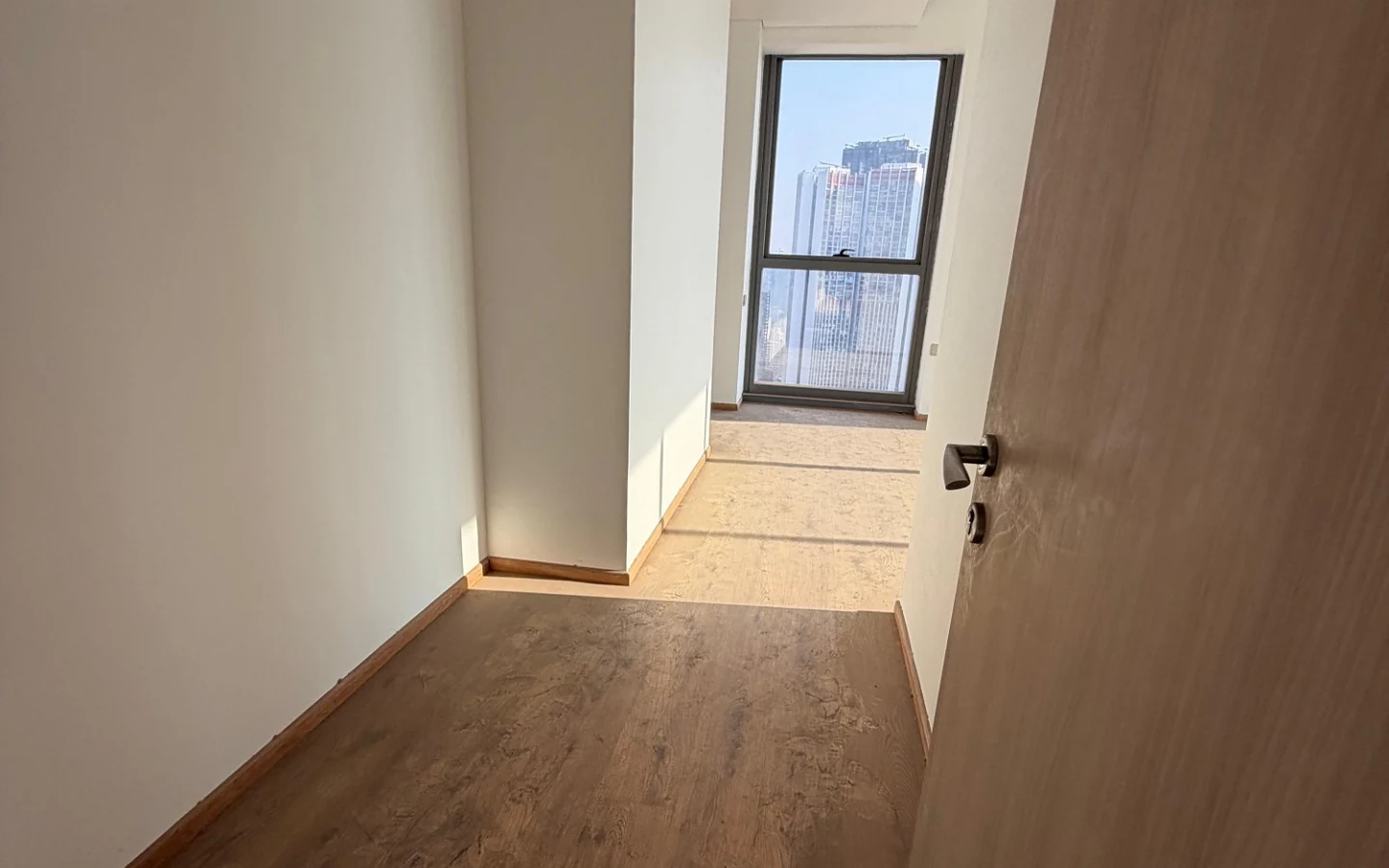 Passage with wooden flooring leading to a floor-to-ceiling window at Rustomjee Crown, Prabhadevi