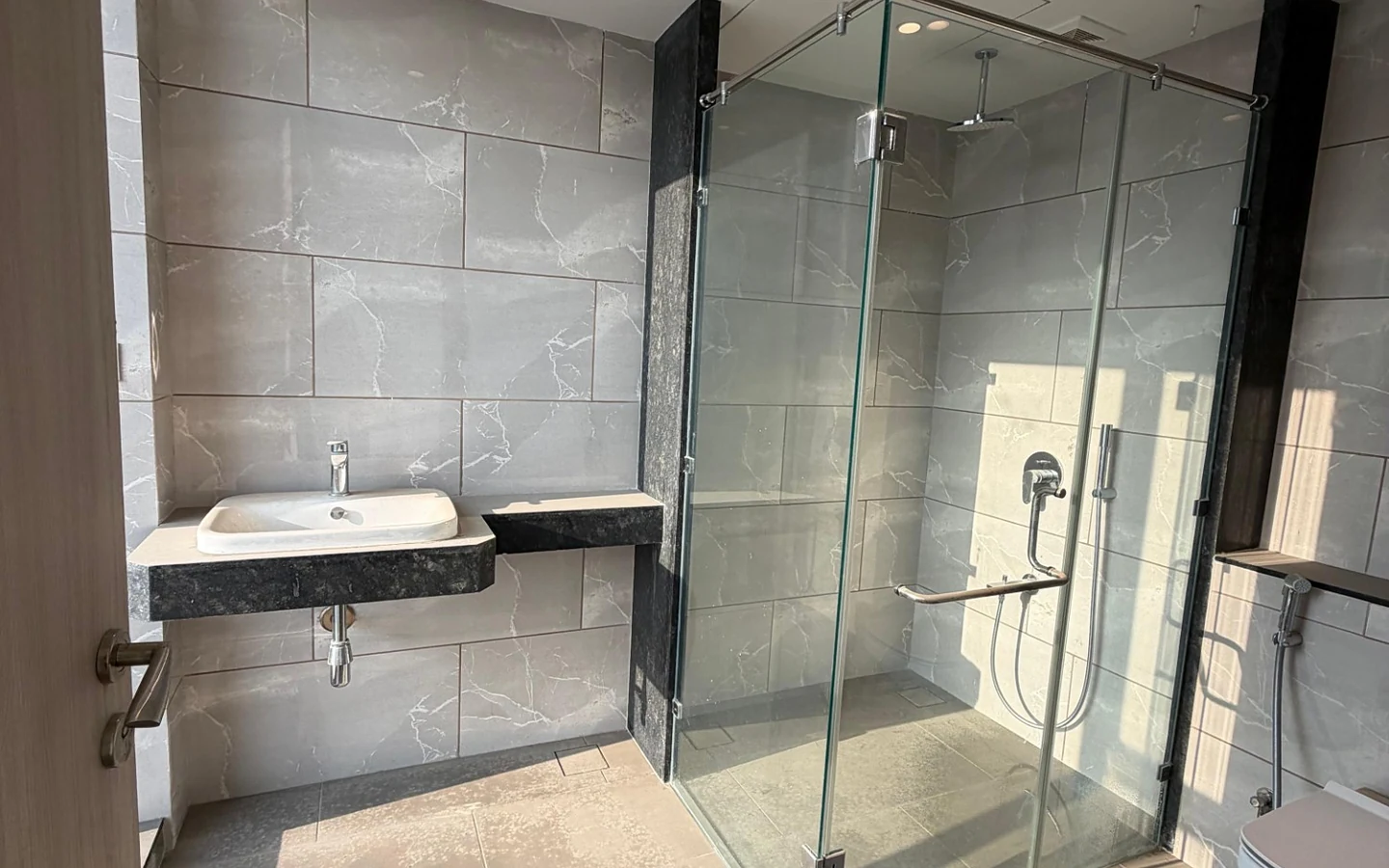 Bathroom with glass shower enclosure, rain shower, granite vanity and wall-hung WC at Rustomjee Crown, Prabhadevi